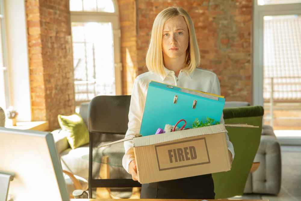 Upset young businesswoman packing office belongings after being fired